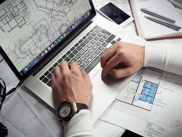 UEBER UNS Architect reviewing detailed floor plans and schematics on a laptop with a smartphone nearby.