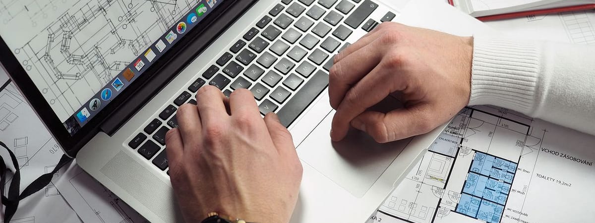 About Architect reviewing detailed floor plans and schematics on a laptop with a smartphone nearby.
